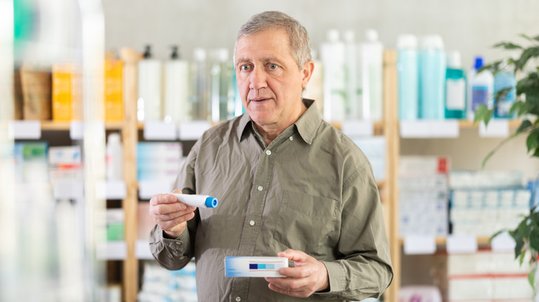 Senior man examining box of ointment while choosing safe medicine for joint or back pain