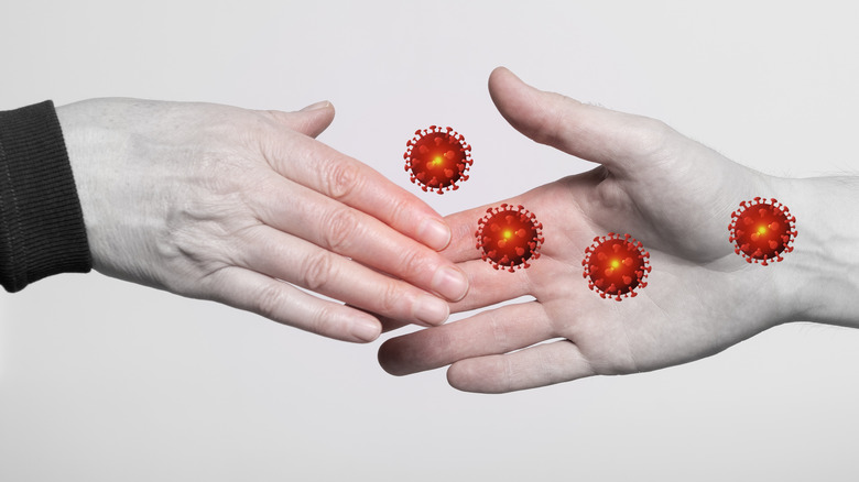 Black and white image of two hands shaking with red virus particles transferring between the hands