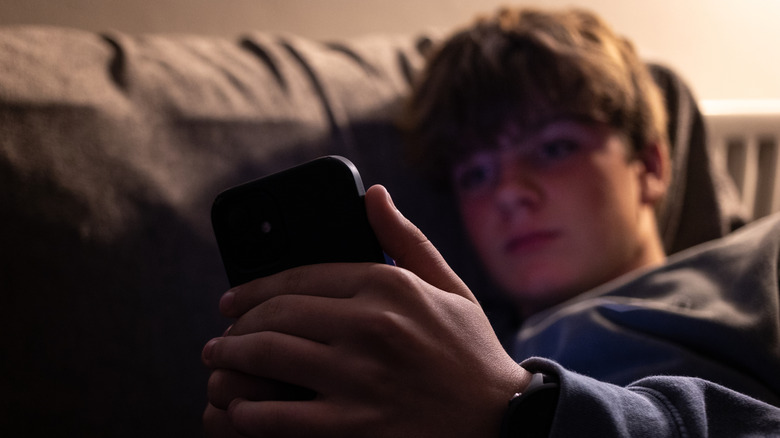A young boy holding a phone and resting his head against a couch.