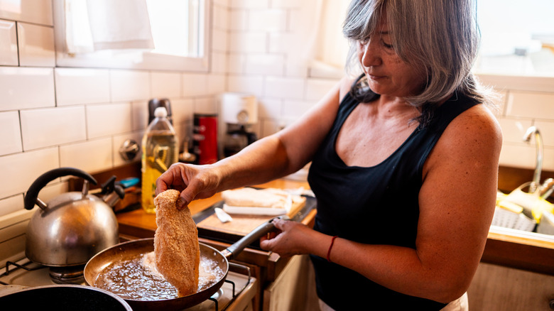 A senior woman cooking a chicken breast at home