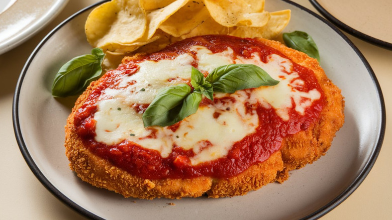 Chicken Parmigiana and potato chips on a white plate