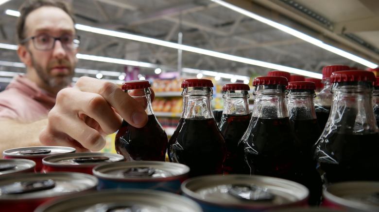 man reaching for a bottle of Coke in a store