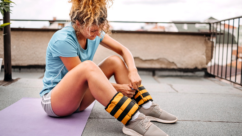 A young woman attaching thick ankle weights before her walk