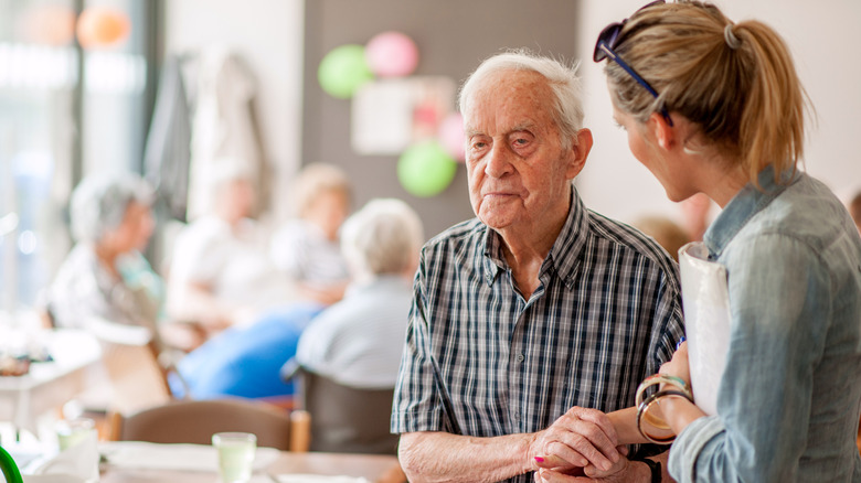A senior man getting assistance from a young woman in a care facility