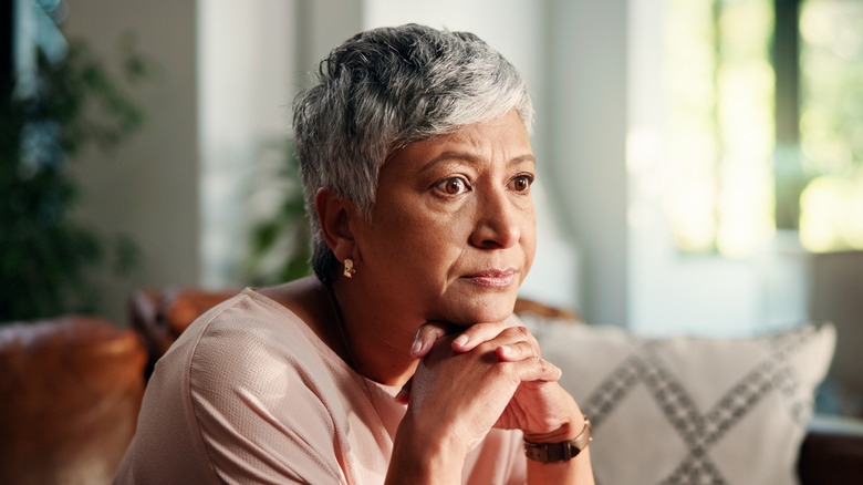 An older woman sitting alone in her room with her hands folded
