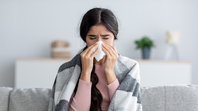 Woman on couch blowing her nose
