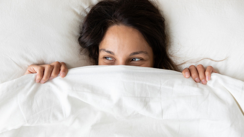 Woman smiling while hiding under her comforter