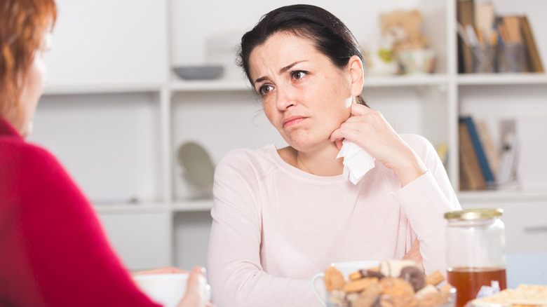 Woman sitting at a table clutching a paper napkin