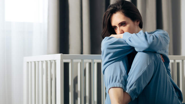 woman sits in front of baby crib