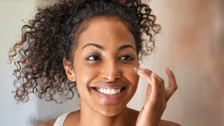 A woman applies face moisturizer
