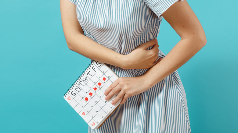 woman holding stomach in pain with period calendar 