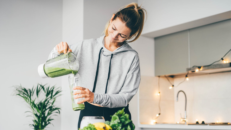 A smiling girl pours a smoothie into a glass