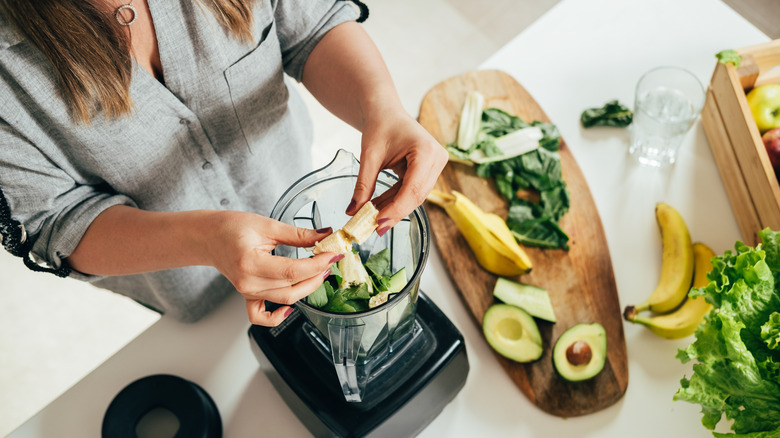 A woman puts a banana in a smoothie