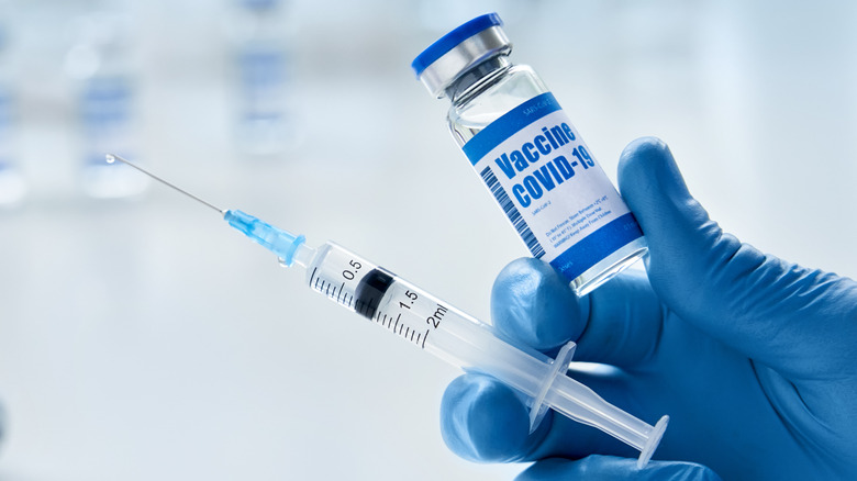 Gloved hand holding vial of COVID-19 vaccine and syringe