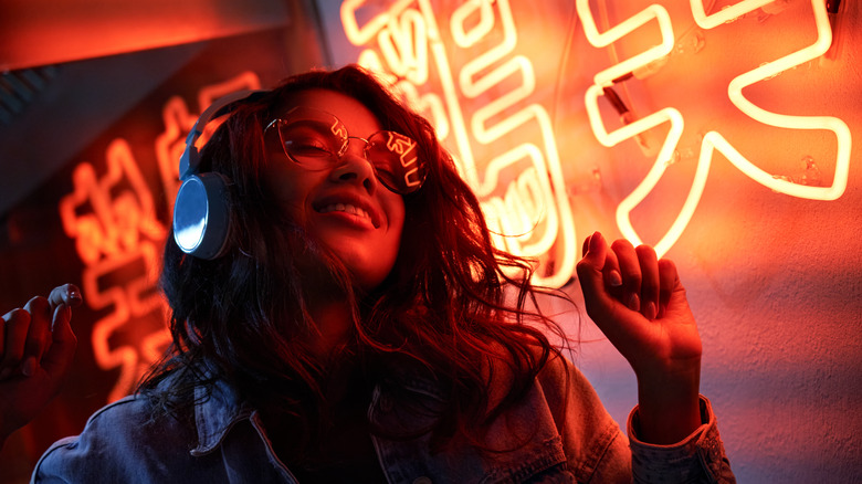 girl with headphones on looking euphoric in front of neon sign
