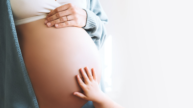 child's hand on pregnant belly