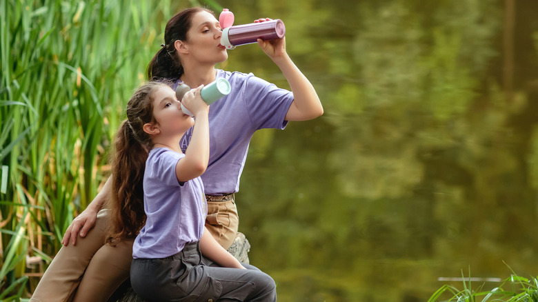 Mother and daughter drinking from water bottles on a hike