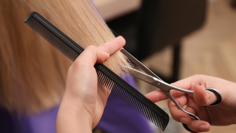 Close-up of hair stylist's hands cutting away at customer's split ends with scissors