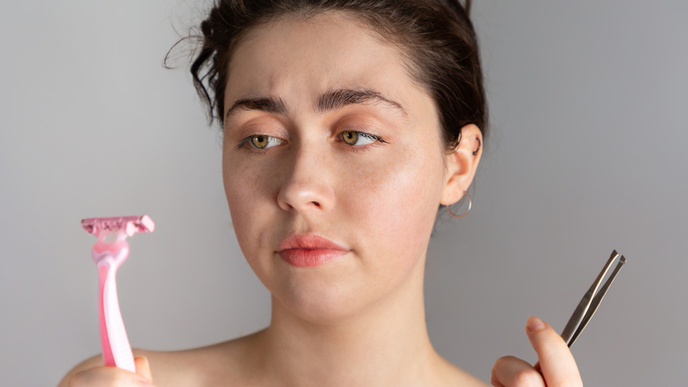 A woman holding up tweezers or a razer  