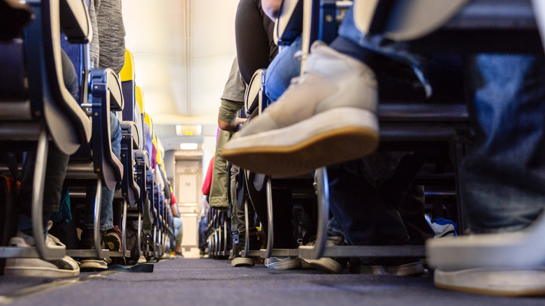 Plane aisle of seated passenger legs and shoes