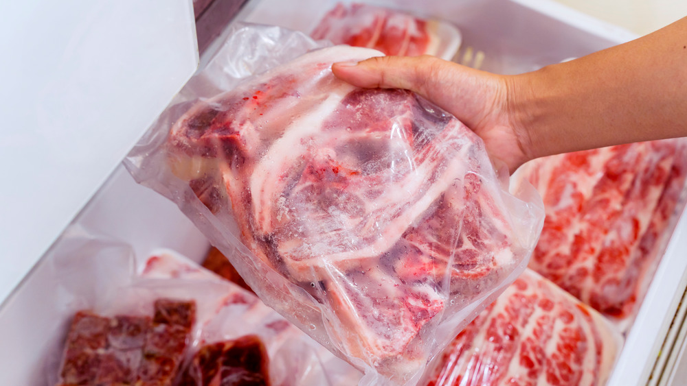 Person's hand pulling a bag of raw red meat out of the freezer