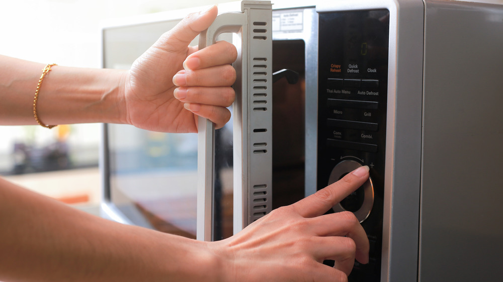 Person pulling a raw chicken on a plate out of the microwave after thawing it