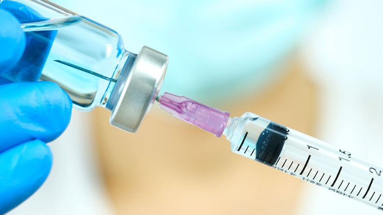 Gloved hand holding vial and syringe