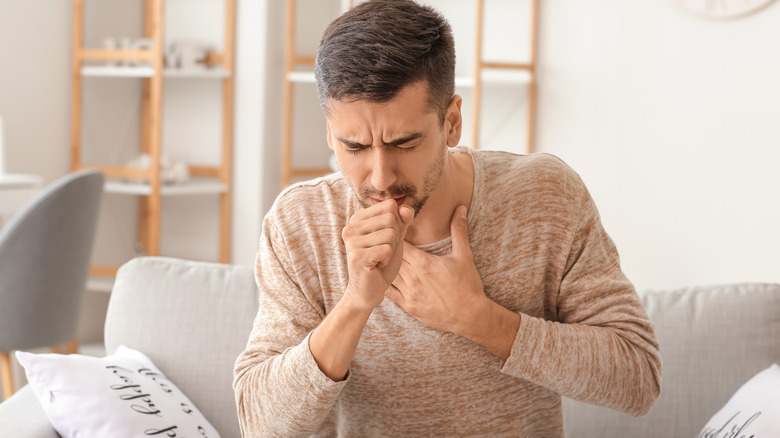 man sitting on couch coughing