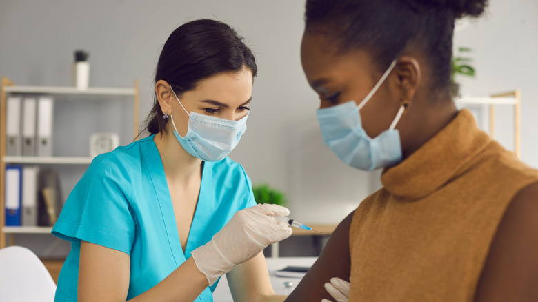 Woman with face mask getting vaccine in arm from nurse