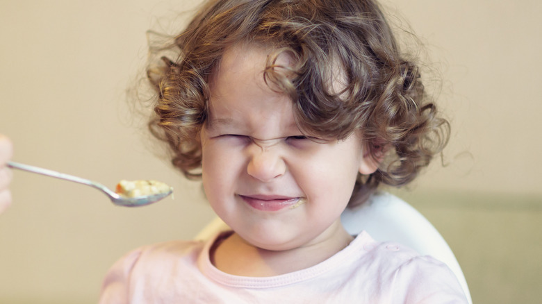 curly-haired toddler grimacing at food 
