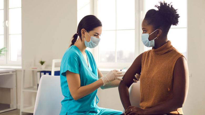 Black woman receiving vaccine by woman doctor