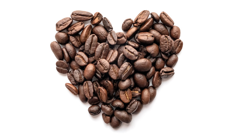 Roasted coffee beans in the shape of a heart on a white background