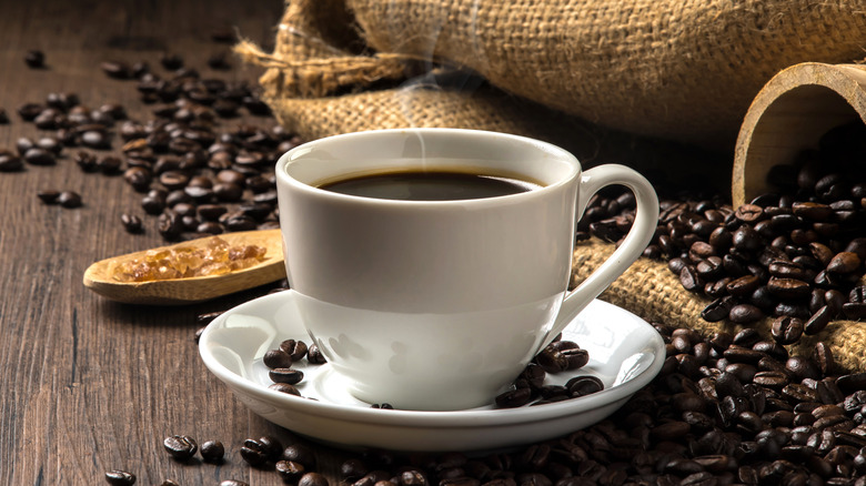 cup of hot coffee surrounded by coffee beans