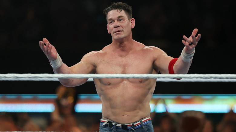 John Cena raises both hands to the crowd in a wrestling ring during a match