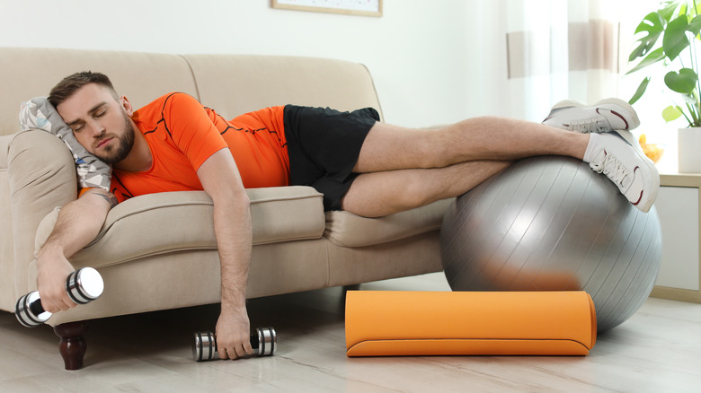 man sleeping on the couch next to exercise equipment