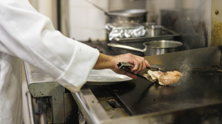 man using tongs in commercial kitchen to cook chicken