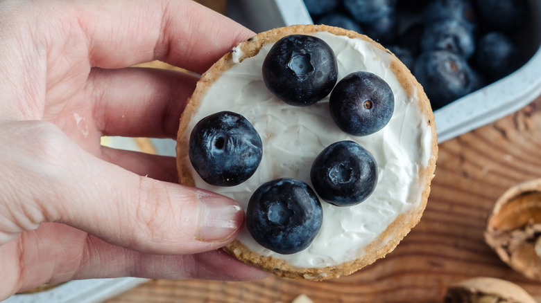 A hand holding a biscuit with blueberries and cream
