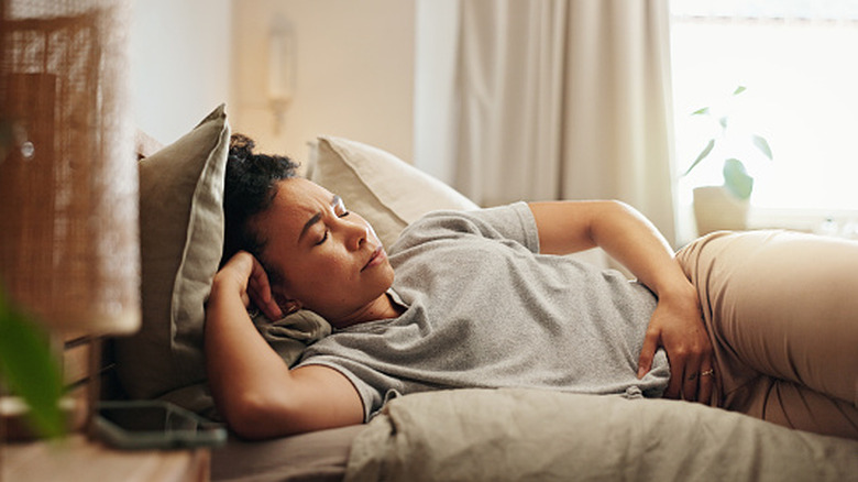 A woman leaning back from a dinner table feeling stomach bloating
