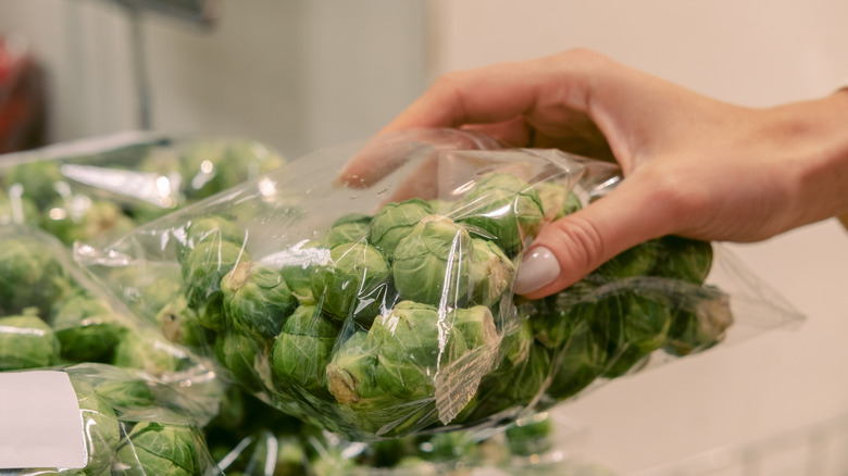 Woman picking up a bag of Brussels sprouts at store
