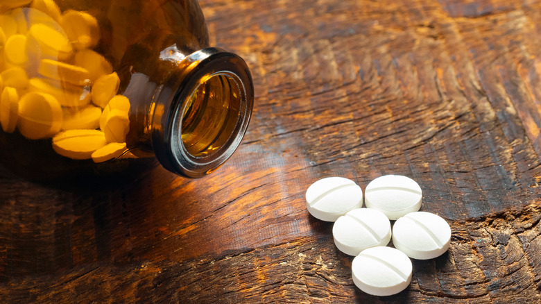 An amber bottle full of aspirin with some pills spilled on the table beside it