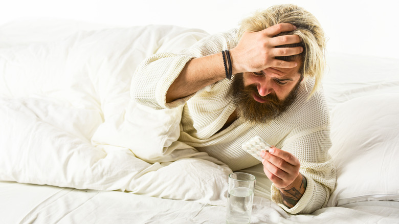 A man waking up with a hangover looking at a pack of aspirin with a glass of water next to him