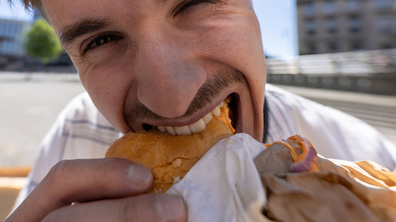 man outside biting into a large sandwich
