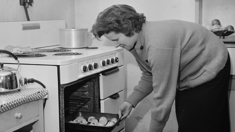 woman taking home cooked meal out of oven in 1950s kitchen