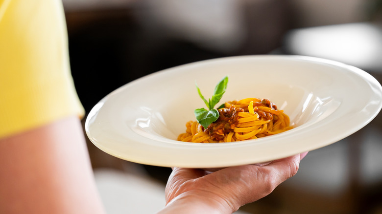 woman from behind holding small portion size of pasta on plate