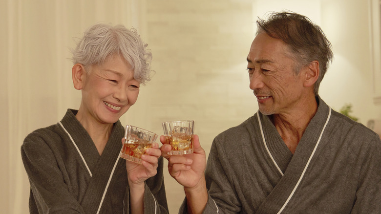 Senior couple toasting with whisky nightcap in hotel bedroom