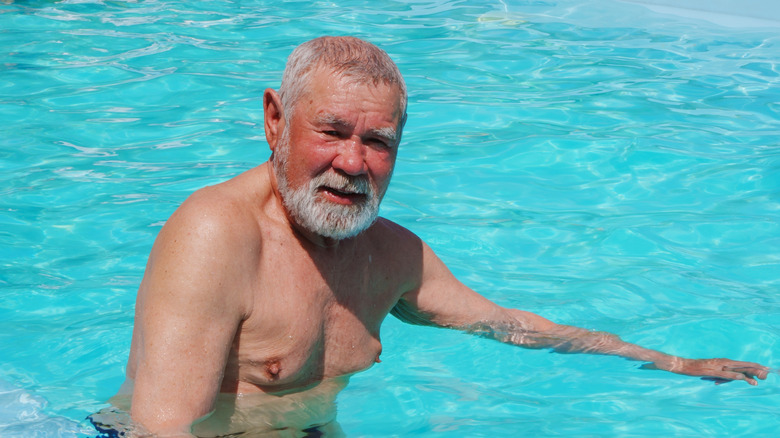 Senior man with tan skin smiling while standing in a pool