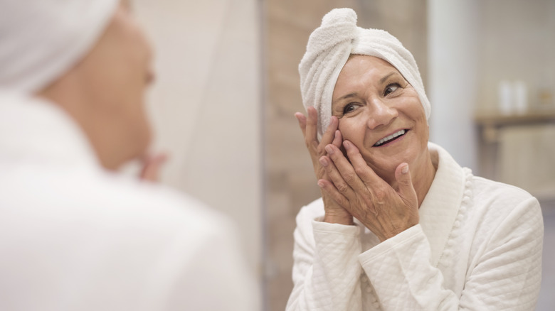 Senior woman looking in mirror while wearing a towel on her head