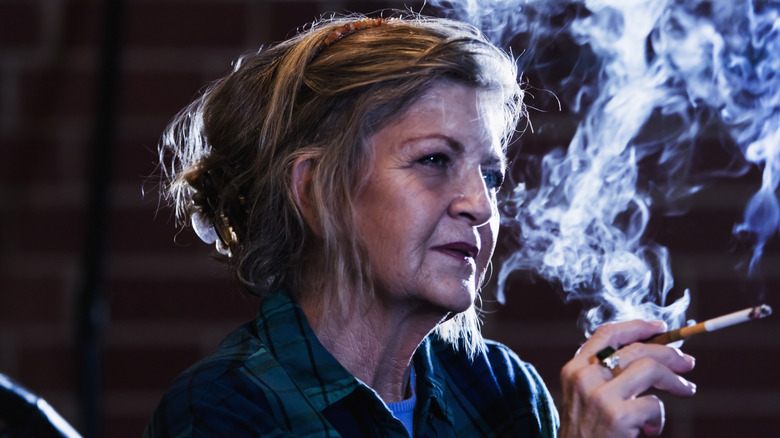 A woman in her sixties smoking a cigarette in a dark room