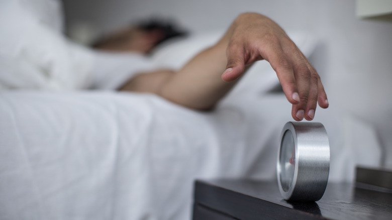 man in bed reaching for his clock
