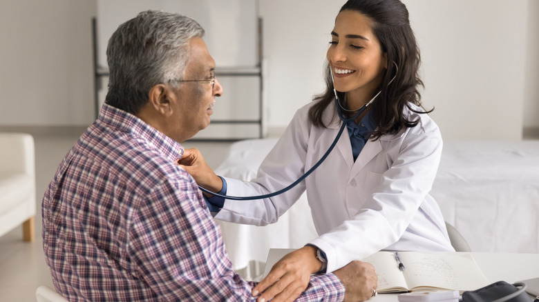 female doctor smiling while checking male patient heart